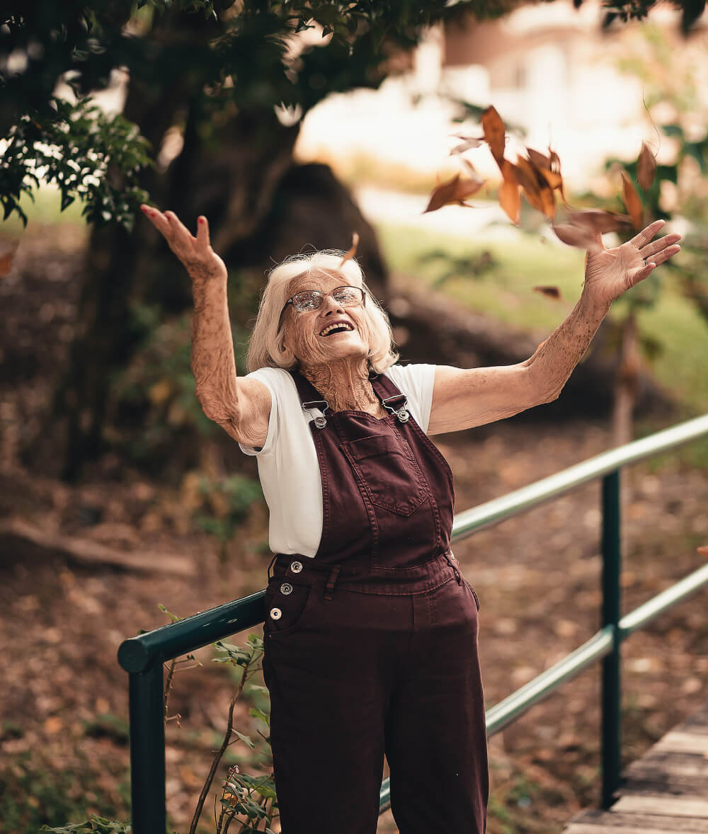 senior woman tossing leaves outdoors